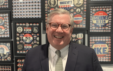 Jim Comerford smiles in front of buttons in his political campaign memorabilia collection.